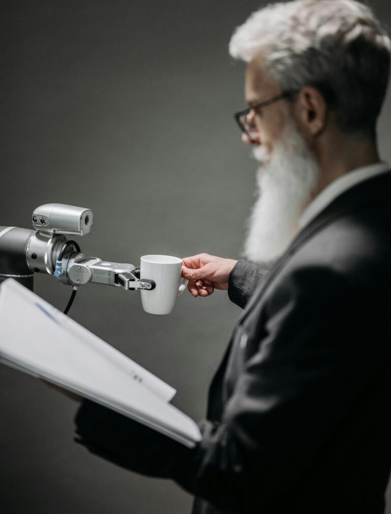 Elderly man interacts with robot arm holding a cup, showcasing innovation indoors.